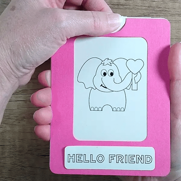 Hand pulling tab on a pink framed Magic slider card to change a black & white elephant to color with a 'Hello Friend' message