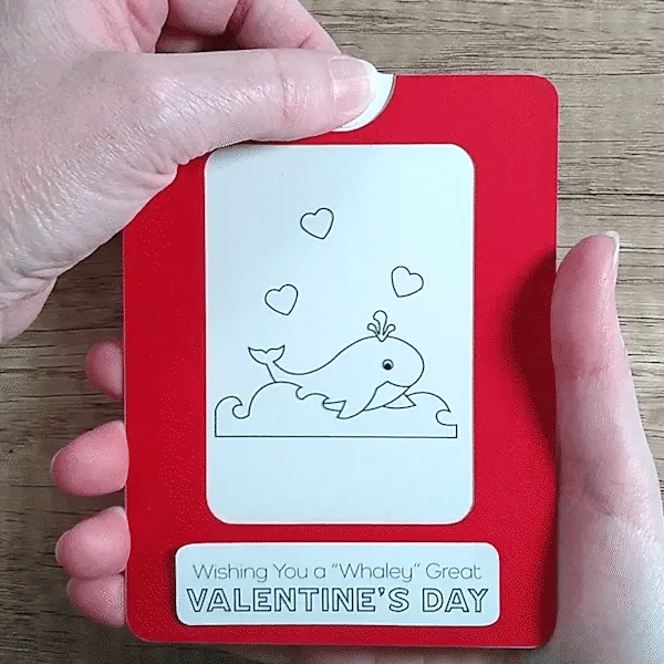 Hand pulling tab on a red framed Magic Slider Card with a whale design and 'Valentine's Day' text.