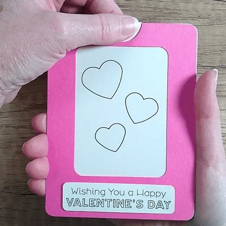 Hand pulling tab on a  pink framed Magic Slider Card with heart designs and 'Happy Valentine's Day' text.