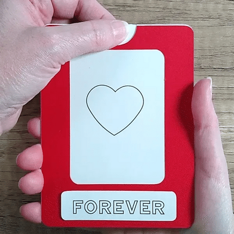 Hand pulling tab on a  red framed Magic Slider Card heart design revealing 'I love you' message.